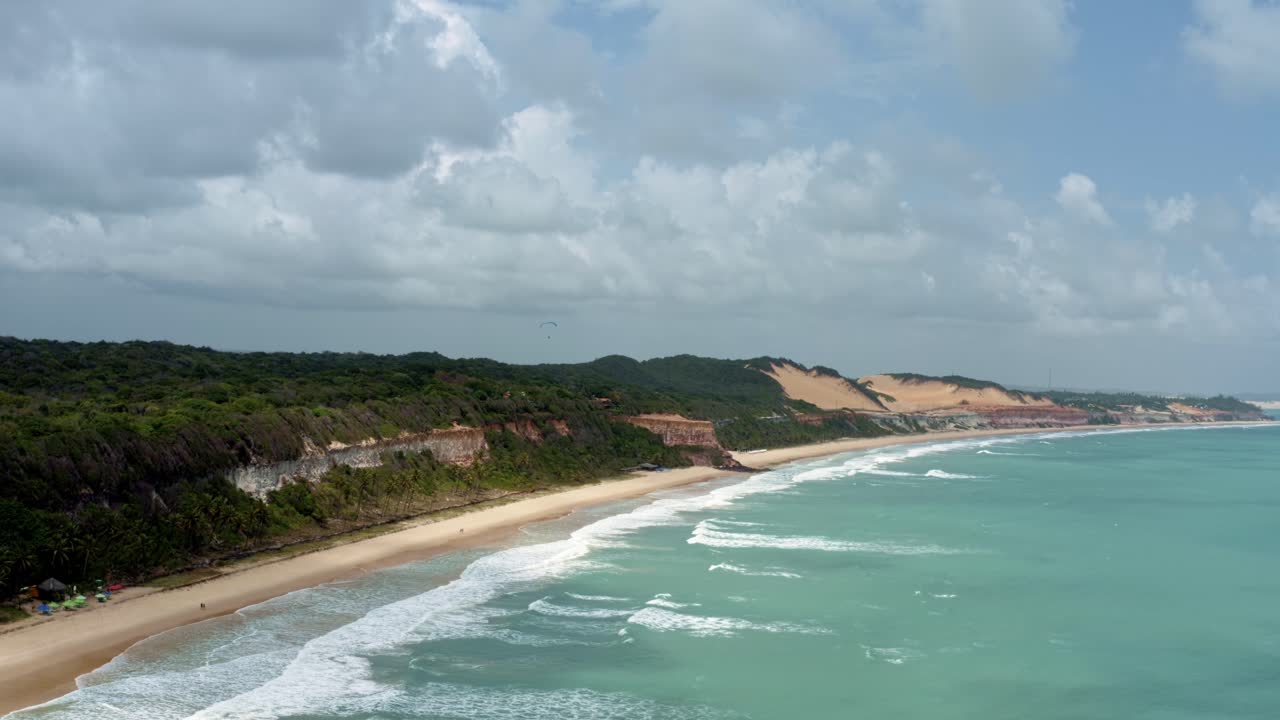 dolly en un dron aéreo giratorio toma de un parapente volando sobre la increíble costa tropical del noreste de brasil cerca de la playa de madeiro en pipa, brasil en río grande do norte con grandes acantilados