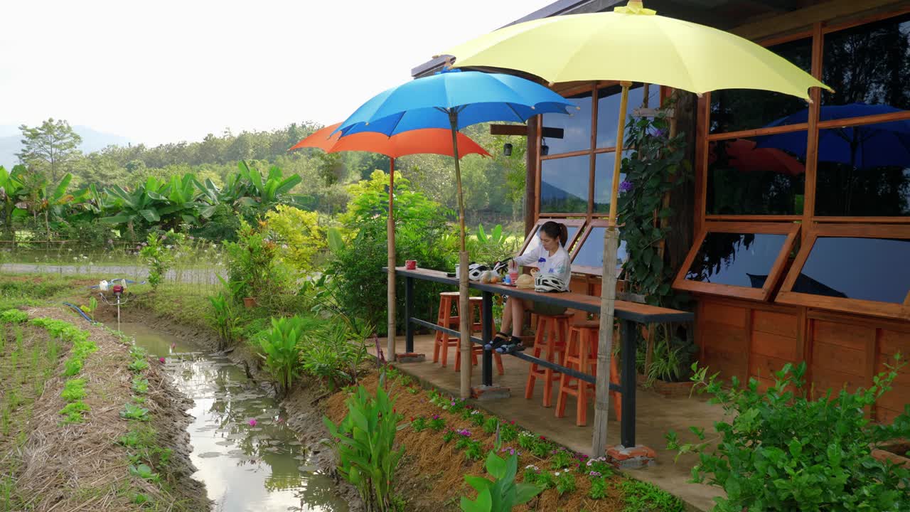 A lone female sits outside at a small rustic local caf&eacute; with colorful umbrellas in a remote part of Nan Province, Thailand