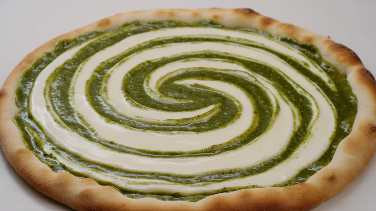 Primo piano di pizza con spirale di pesto, spirale lucida di crema e pesto al basilico, crosta dorata e cotta, illuminazione da studio.