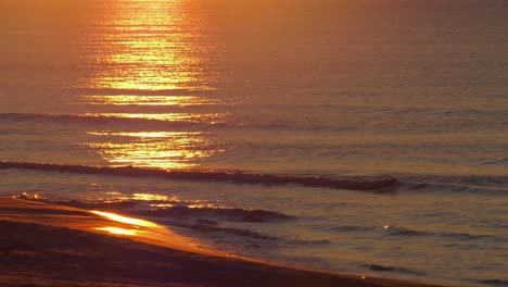 waves on sandy beach reflecting sunrise, slow motion