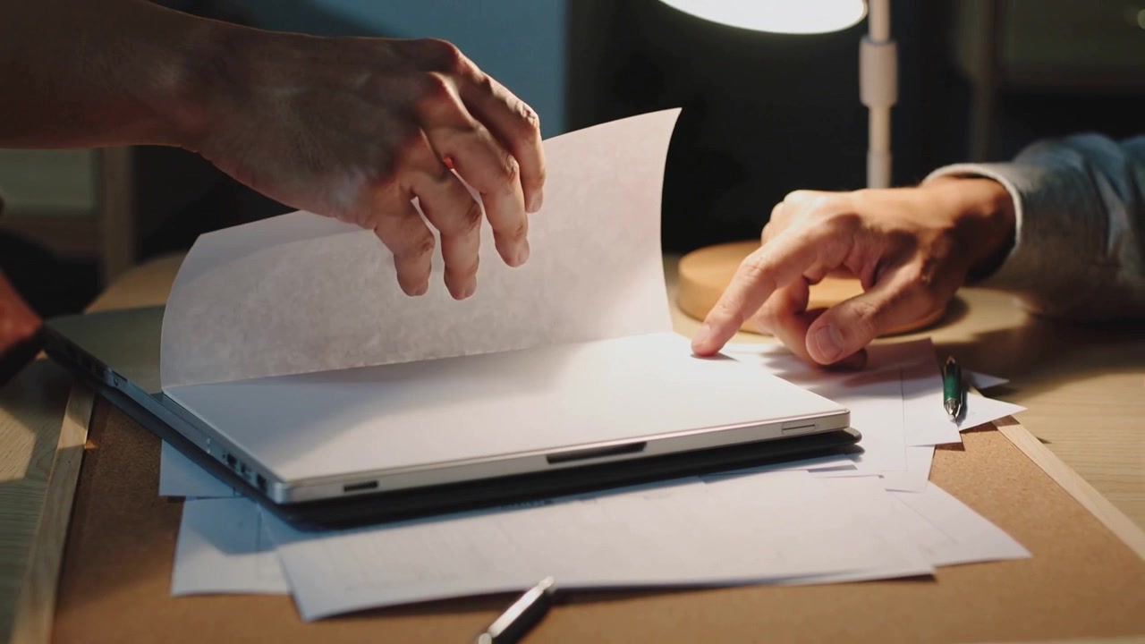 Lifting hand turning sheet over thin laptop at desk pointing hand marking spot wearing long sleeves