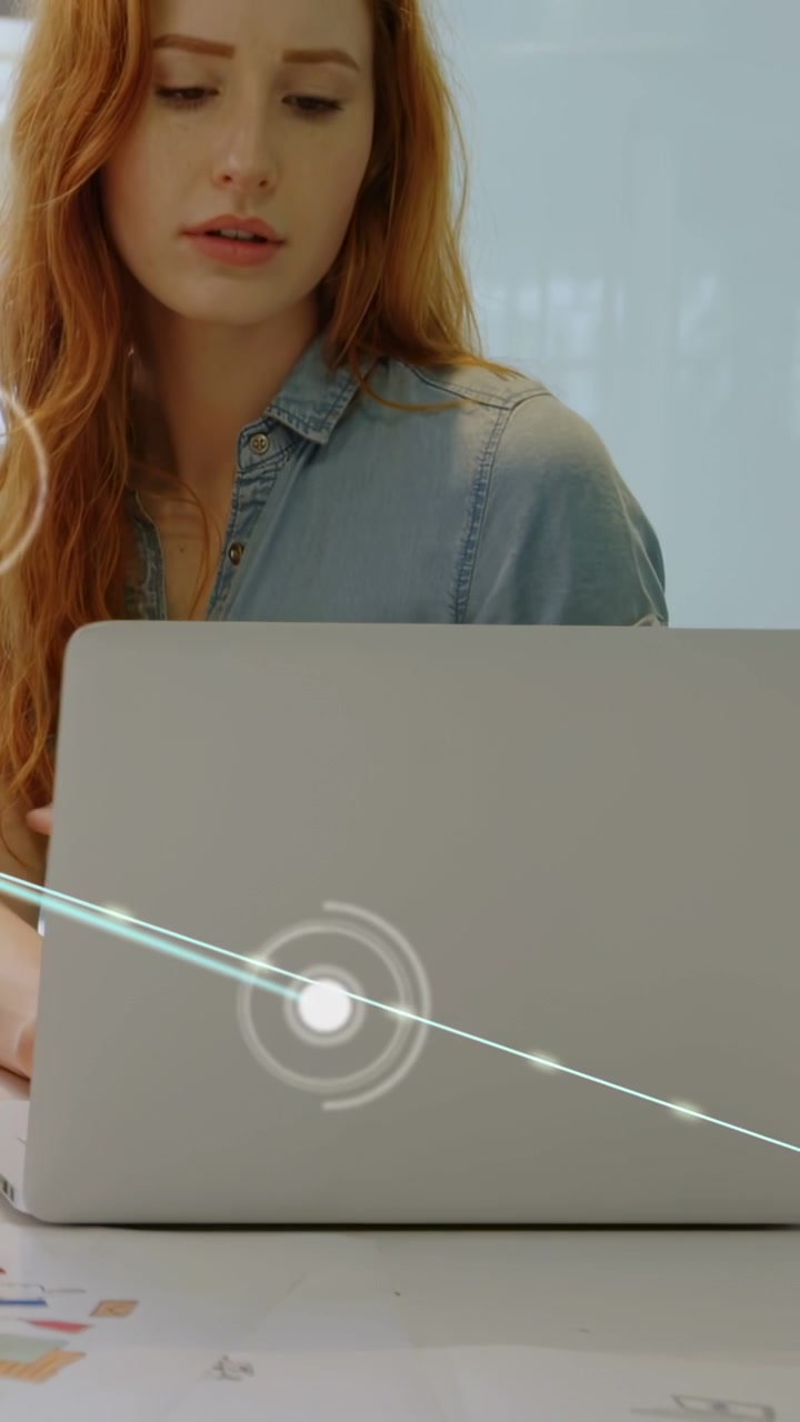 Video verticale: Donna seduta al laptop, osserva un HUD emergere in basso a sinistra e scansionare dati tecnologici.