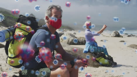animación de células de covid-19 flotando sobre una pareja mayor con máscara facial y mochila en la playa