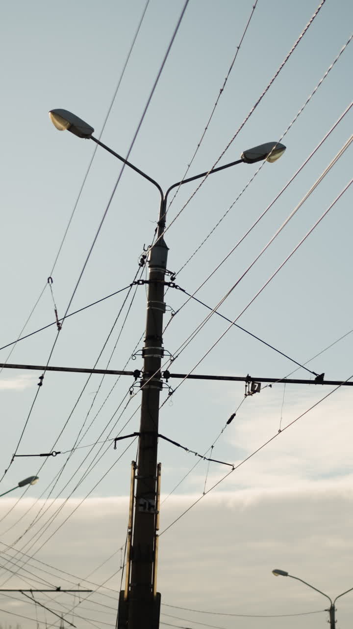 twin streetlights under crisscrossing wires dusk, layered cables stretching across soft evening sky, distant horizon and cloud band, industrial silhouette and calm atmosphere, municipal inspector
