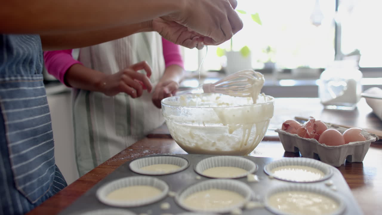sección media de madre y hija biraciales horneando, preparando mezcla de pasteles en la cocina, cámara lenta