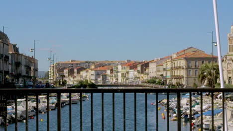 Sunny day view of Sète canal lined with boats and colorful old buildings under blue sky