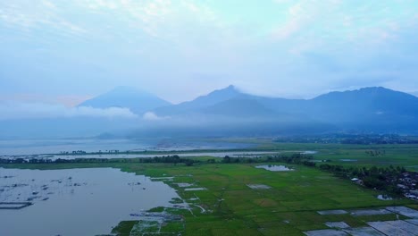 Tiro-De-Drone-De-Campo-De-Arroz-Y-Lago-Con-Cordillera-En-El-Fondo