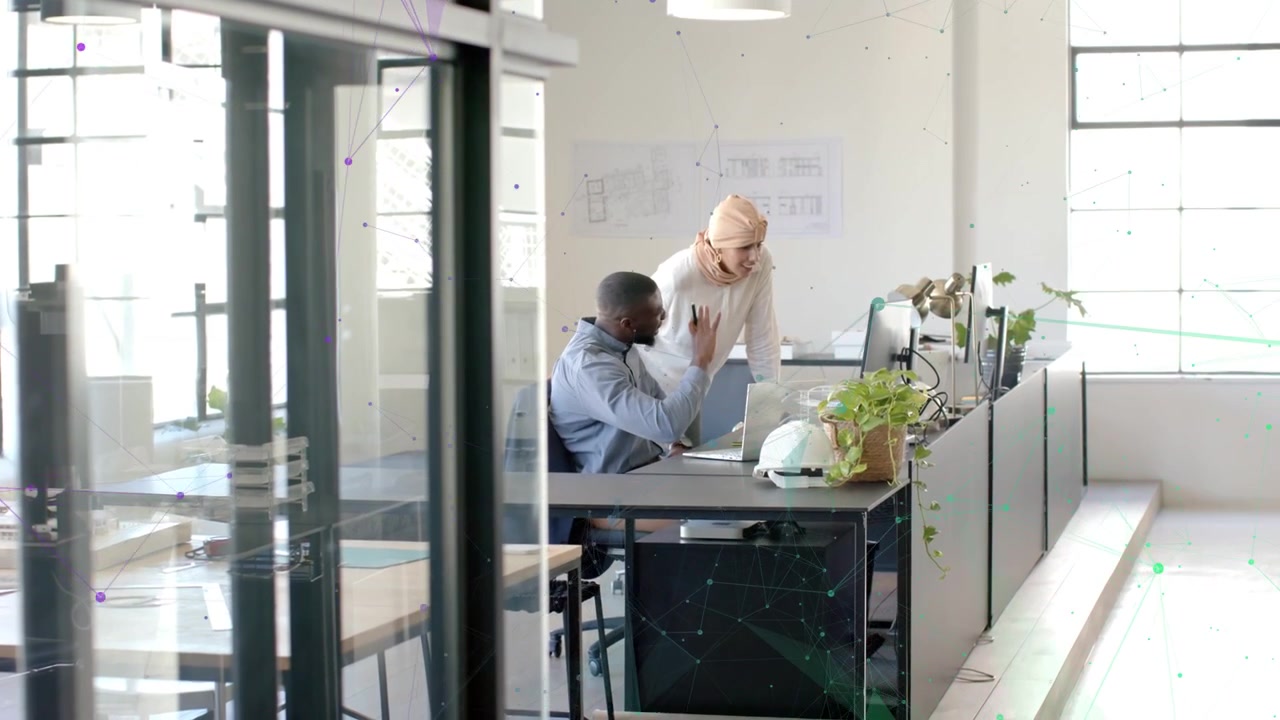 Standing woman leaning in, starting monitor review while man pointing at plans, reviewing design