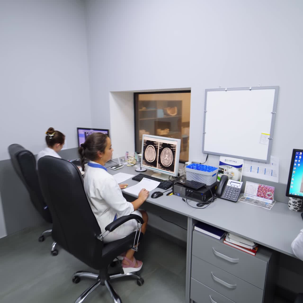 Smiling female lab technician stands up from a table and leaves the room. Modern room for magnetic resonance scanning in hospital