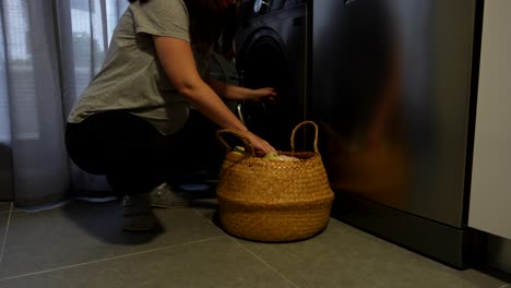 pregnant woman loads baby clothes into washing machine at home, soft and calm moment