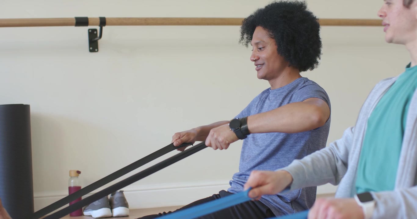 Two African American men sitting on purple mats, looping bands on feet, pulling for fitness