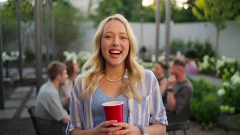 Portrait-of-a-happy-cheerful-blonde-girl-in-a-blue-shirt-posing-and-laughing-while-relaxing-with-her-friends-in-the-courtyard-of-a-country-house