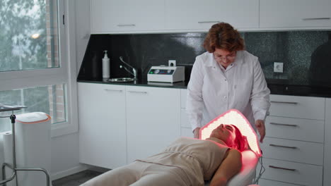 cosmetologist making lamp treatment for woman lying couch beauty clinic.