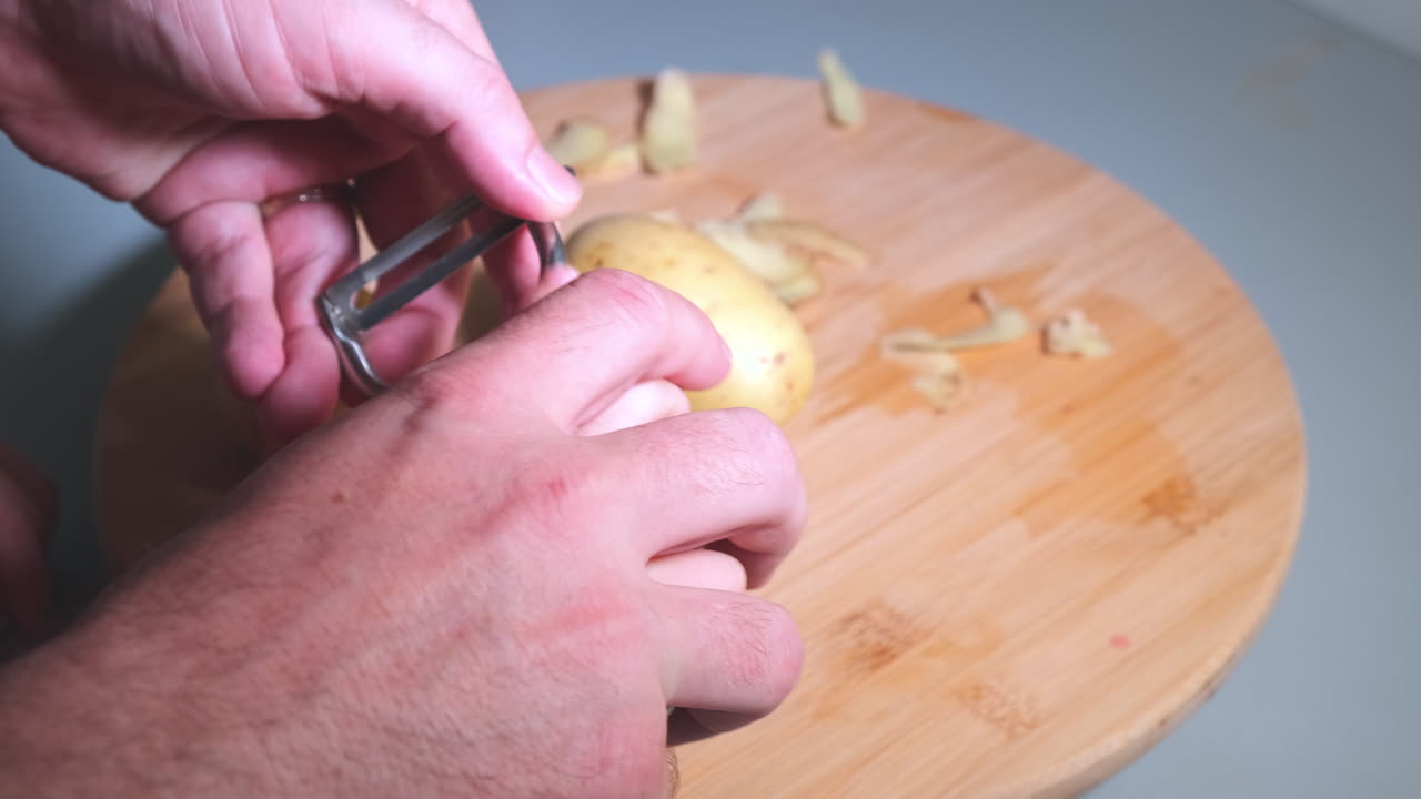 Hands of father and daughter holding peeler and peeling potatoes, parents teaching children basic skills