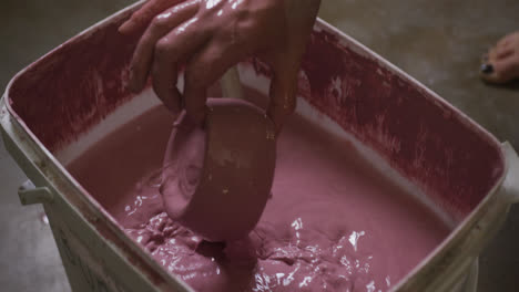 Close-up-view-of-female-potter-dipping-pot-into-paint-at-pottery-studio