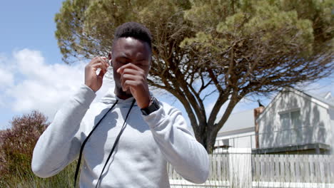 Happy-african-american-man-using-headphones-and-smartwatch-on-street-on-sunny-day,-slow-motion