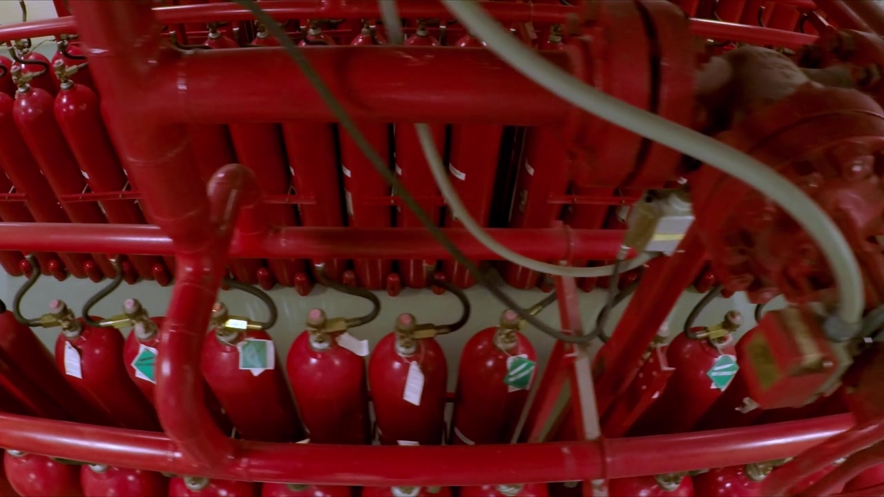 File di bombole antincendio rosse collegate tramite un sistema di tubazioni industriali all'interno di una struttura organizzata per la sicurezza e la protezione.
