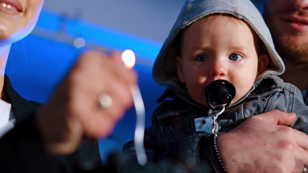 Lovely kid with a pacifier in mouth watches the burning candle on the cake. Low angle view. Family celebration.