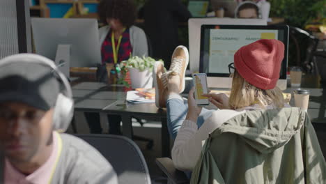 young business woman using smartphone browsing project information on mobile phone screen reading research study statistics brainstorming ideas relaxing feet on table in modern office