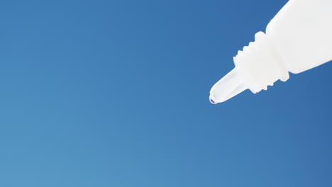 video of white dropper bottle releasing drop on blue background with copy space
