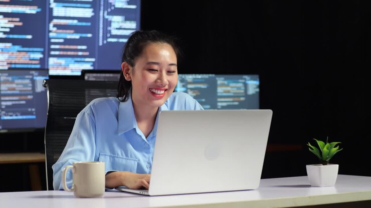 азиатская программистка проводит встречу на ноутбуке во время написания кода на нескольких мониторах, показывая базу данных на десктопах окон терминала в офисе
