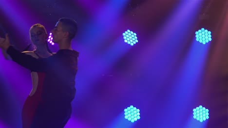 couple performing ballroom and latin dance on stage with colorful lights