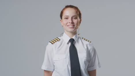 studio portrait of smiling female airline pilot or ship captain against plain background