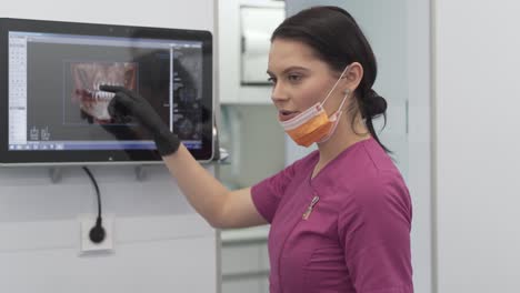 Female-Dentist-in-Her-Uniform-and-Gloves-in-Modern-Dental-Clinic-Showing-Scans-Details-on-Monitor-to-Her-Patient