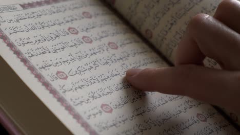 close up shot of a quran and a female person tracing the verses in the quran with her finger, flat version