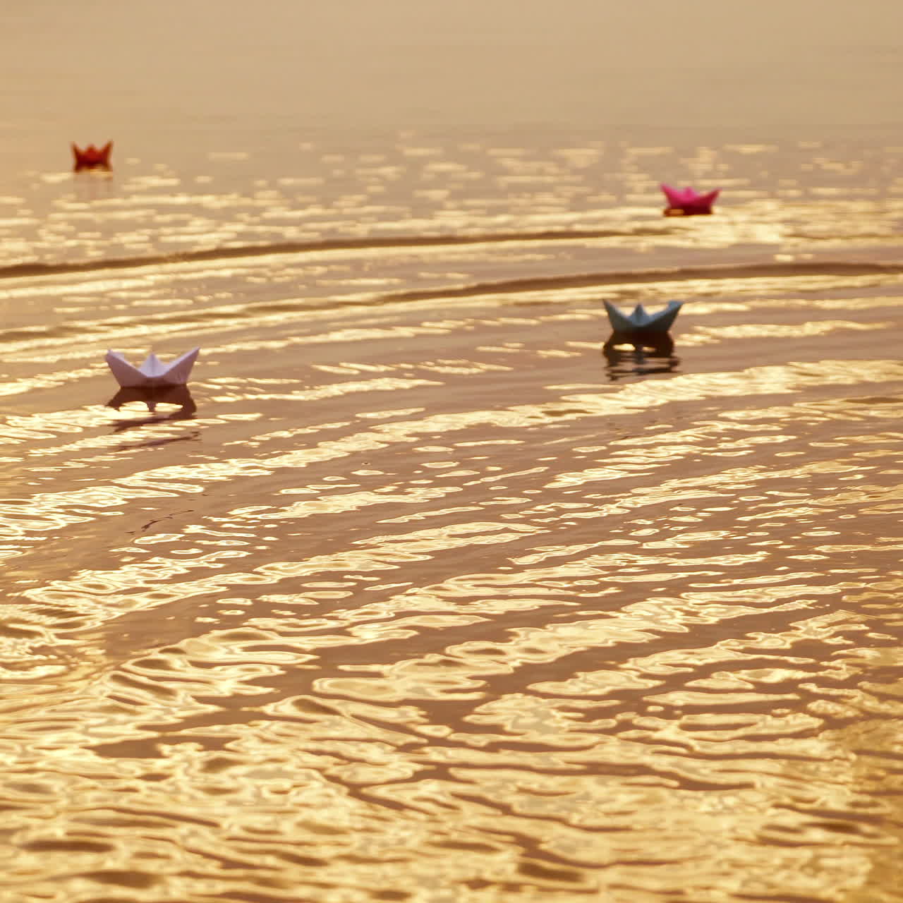 Multy-colored paper boats floating on waves in a river at the evening sunset. Small ships made from paper sail in water.
