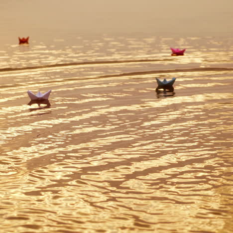 multy-colored paper boats floating on waves in a river at the evening sunset. small ships made from paper sail in water.
