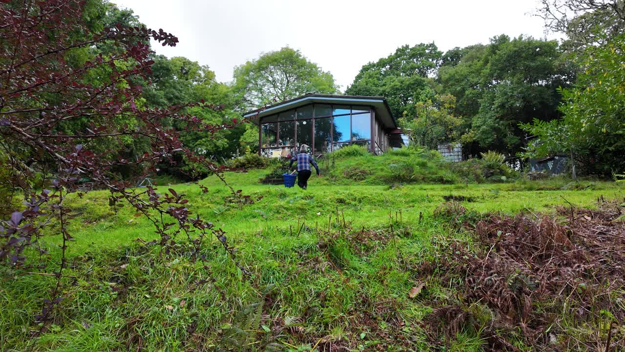 Man running uphill carrying firewood and an axe toward a secluded cabin