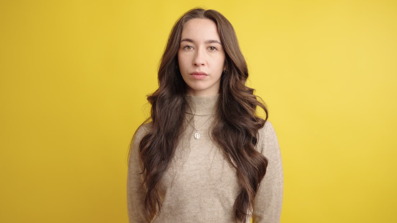 Serious young woman posing on yellow background