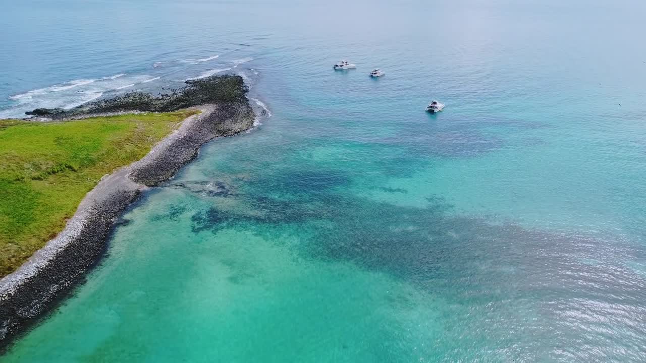 Barriera corallina e barche ancorate a supporto di tour subacquei nel Parco Nazionale Marino di Abrolhos vicino a Caravelas, Bahia, Brasile, con acqua bassa turchese e bordo della barriera corallina, ripresa con drone in volo in avanti