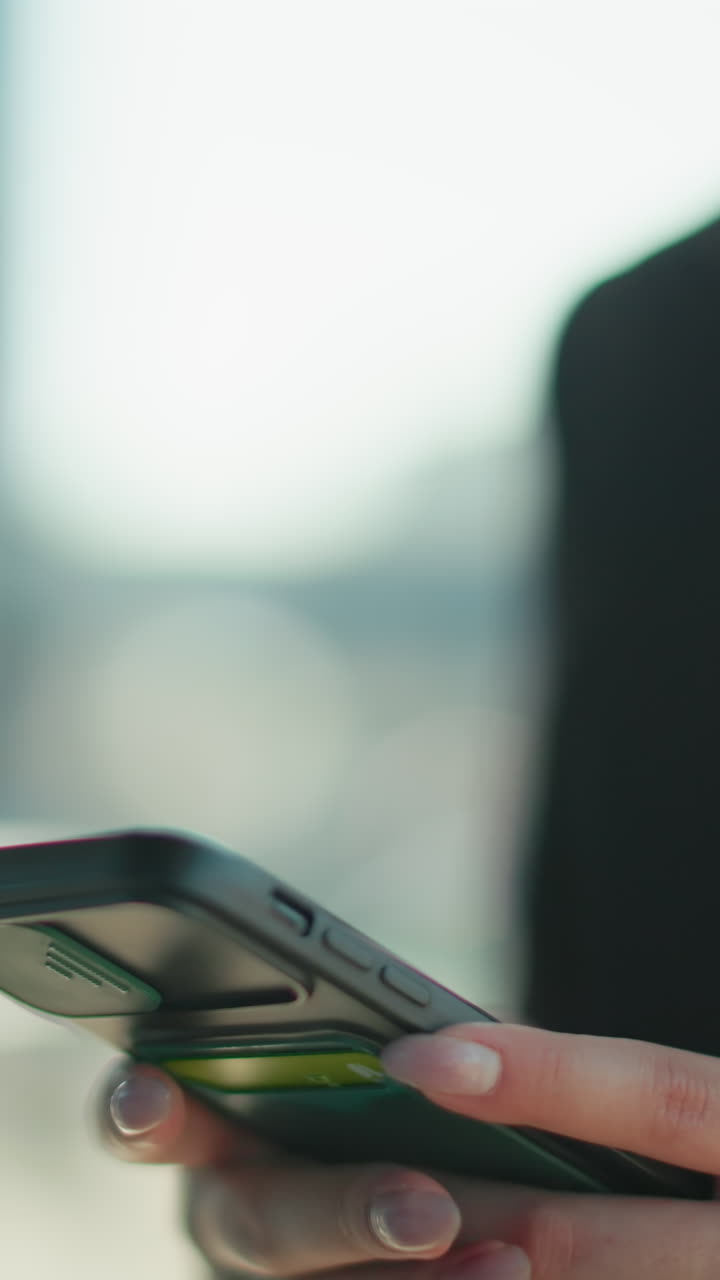 Close-up of woman typing on phone, focused and professional in business attire, urban setting with blurred building background and someone exiting the building