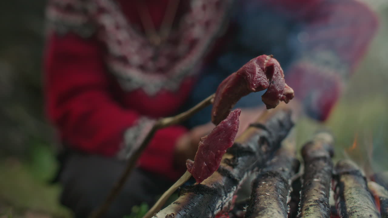 Close Up of Man Roasting Raw Meat on Wooden Sticks over Fire Flame Outdoors