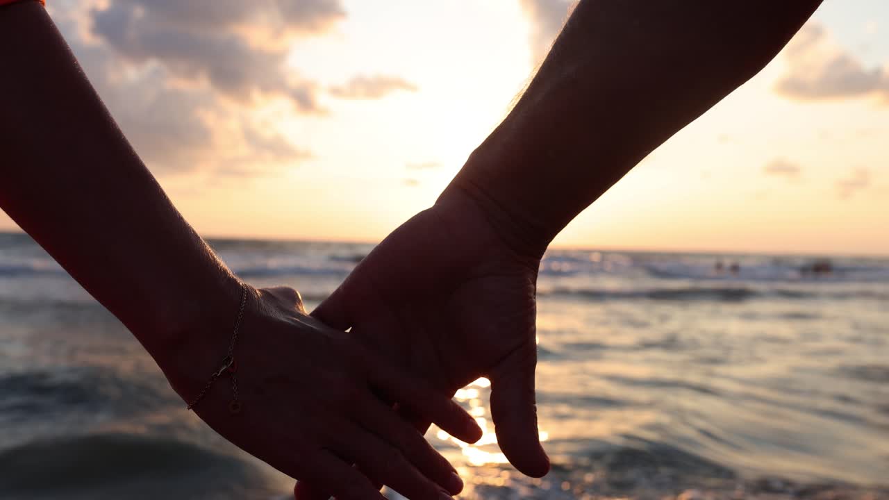 pareja tomados de la mano en la playa al atardecer