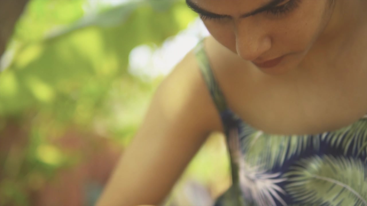 Women gardening closeup with view from down up see leg arm head face and palm tree. She works concentrated with soft light on her.