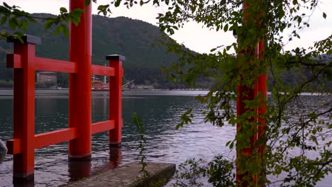 sideways view of red torii gate at hakone shrine with famous pirate ship passing