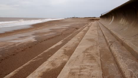 waves-rolling-onto-Ingoldmells,-Skegness-sandy-beach-with-sea-defence-and-wind-turbines-on-the-horizon