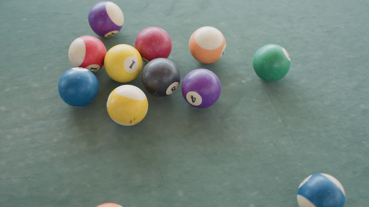 Billiard balls on green felt clustered in triangle rack then scattering after break colorful numbered solids and stripes rolling across textured table surface overhead closeup capturing motion