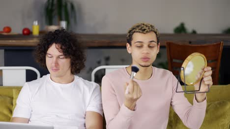 dos amigos gays sentados en el sofá, un tipo rizado haciendo maquillaje en casa