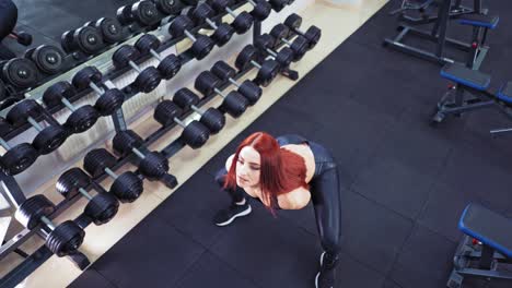 Woman with kettlebell in sports center. Top view of athletic sportswoman lifting and swinging heavy weights in both hands indoors on dumbbells background.