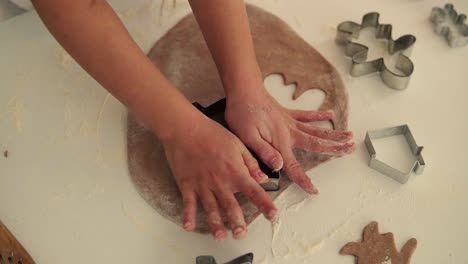 Top-view-of-child's-hands-making-traditional-Christmas-cookies.-Raw-dough-and-cutters-for-holiday-cookies-on-the-white-table---making-fir-tree-shaped-cookie