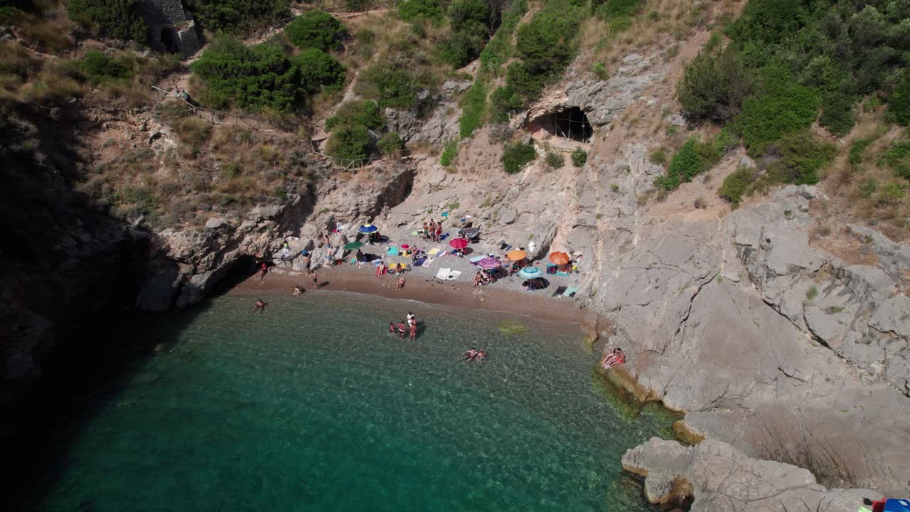 Aerial forward view of a beautiful rocky bay with people in the shore. Salerno. Italy