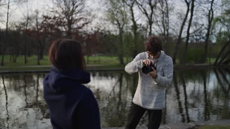 Outdoor-photo-shoot-near-park-pond,-female-pose-in-front-of-photographer