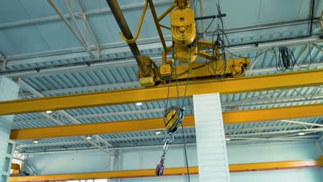 movement of an electric crane along the guide rails under the ceiling into the factory room. dangling large yellow crane hook