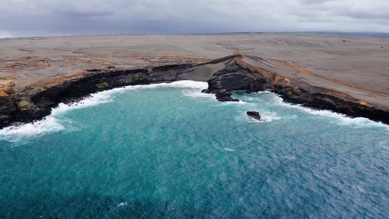 Vibrant turquoise waves fill a wide bay bordered by rare green sand beaches and stark volcanic cliffs in Hawaii, showcasing the dramatic contrast between ocean and barren land.