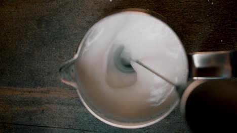 top view coffee creamer with electric milk frother stick going in to and mixing milk on dark background