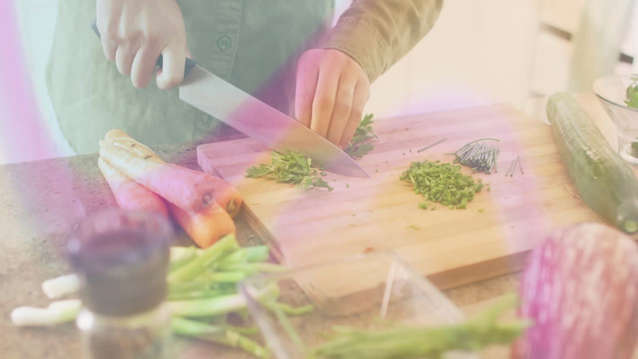 Home cook placing herbs on kitchen cutting board and rocking chef knife, chopping herbs for cooking